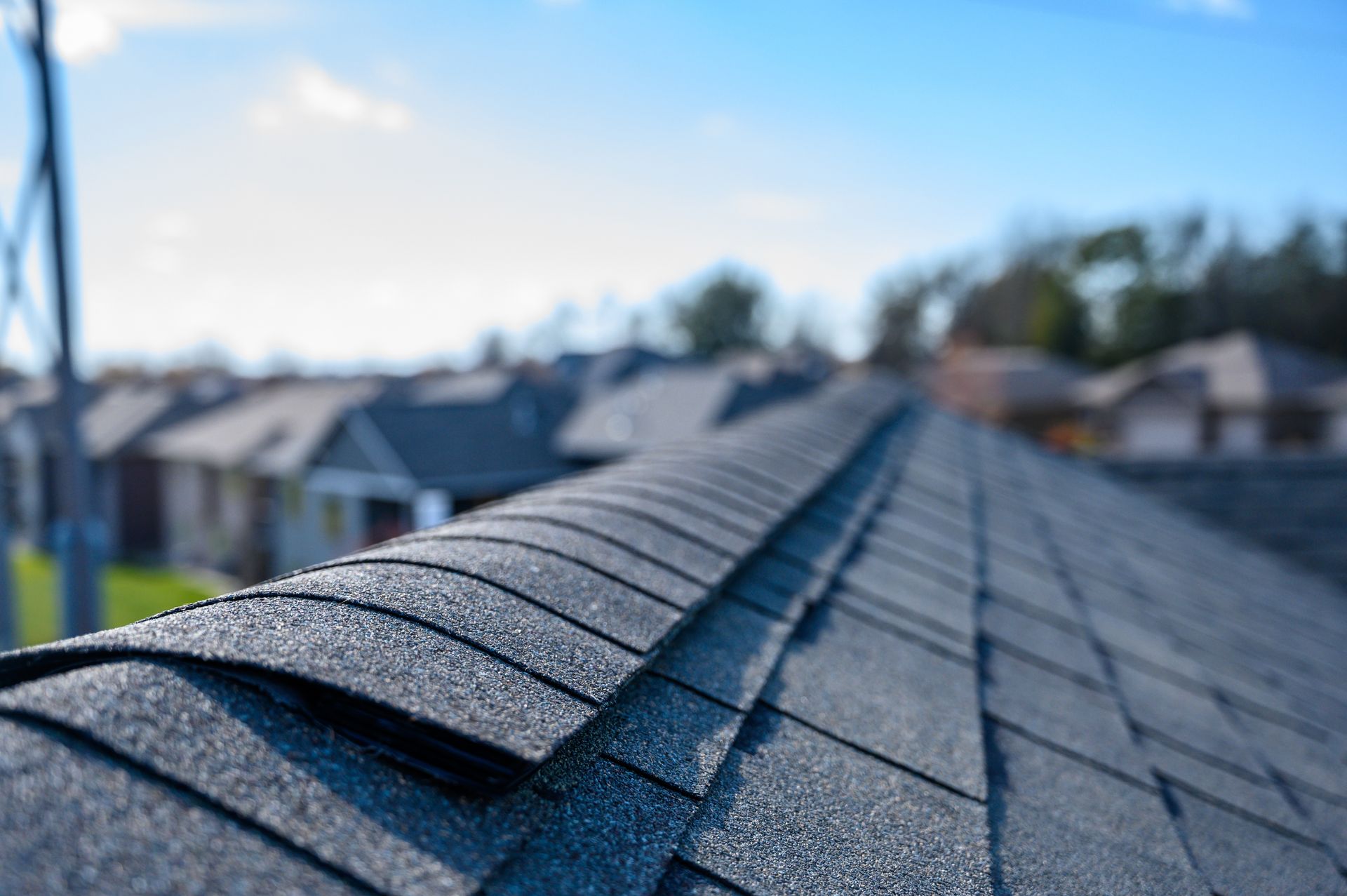 Close-up of asphalt shingles along a roof edge with homes blurred in the background.