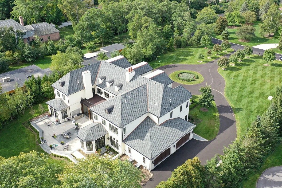 Large brick house with gray roof and shutters, surrounded by green lawn and trees.