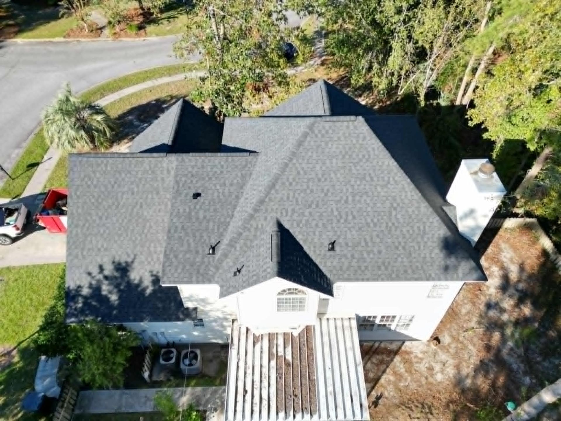 Overhead view of a house with a dark gray shingle roof, white trim, and a yard with trees.