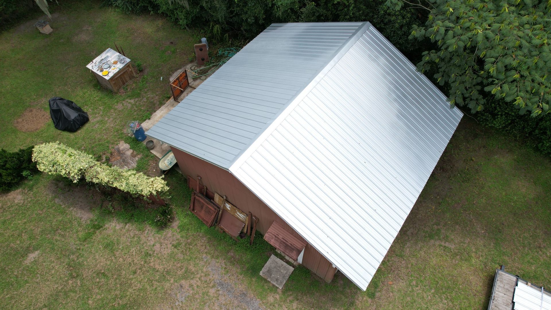 A small brown shed with a silver metal roof sits on a grassy yard.