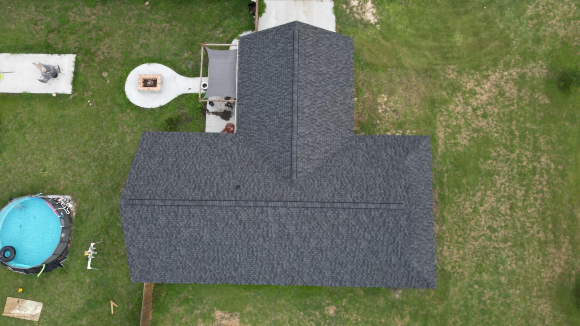 Overhead view of a house with a dark gray shingled roof, set on a green grassy lot.