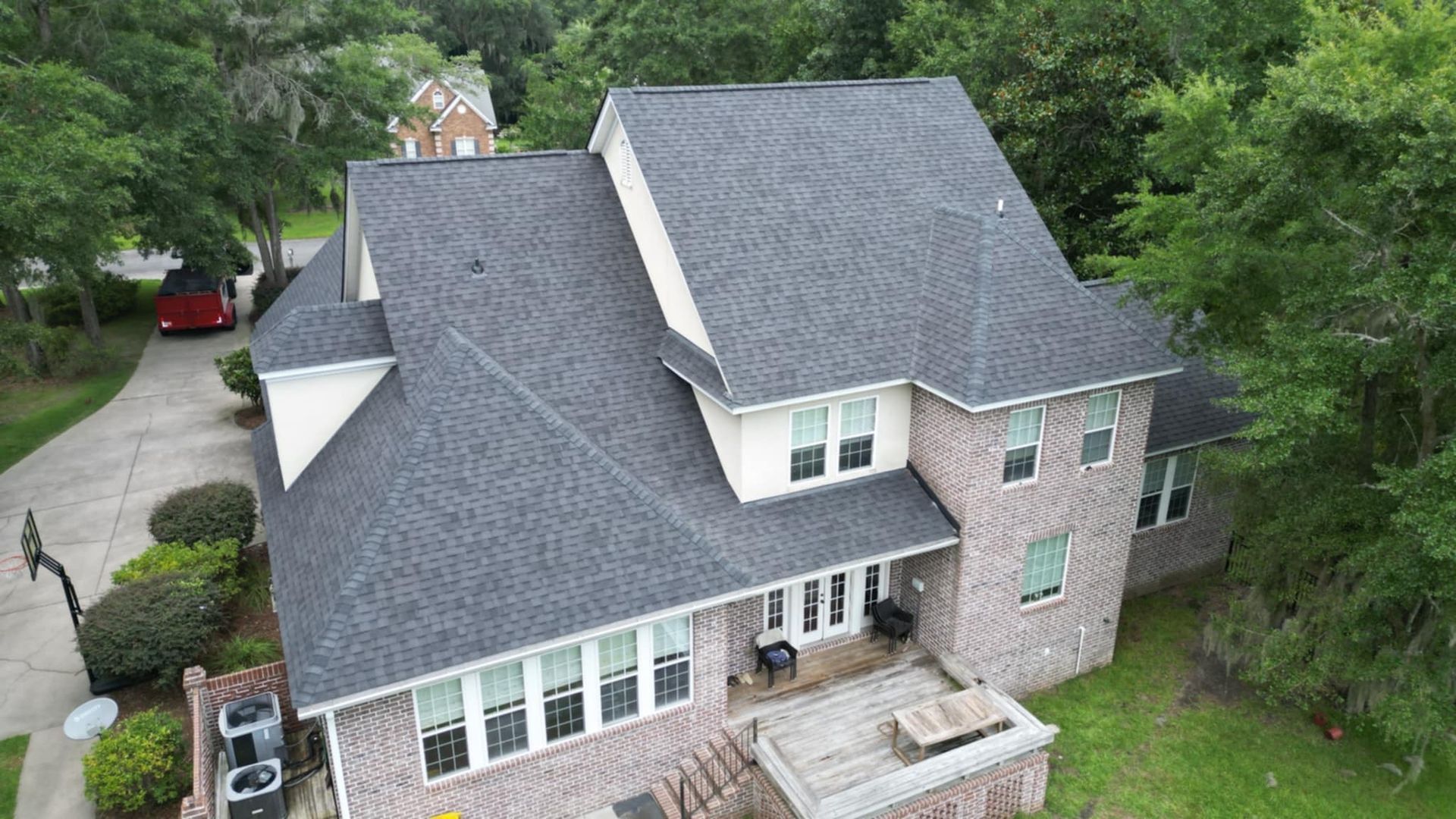 Brick house with dark gray roof, surrounded by trees and greenery.