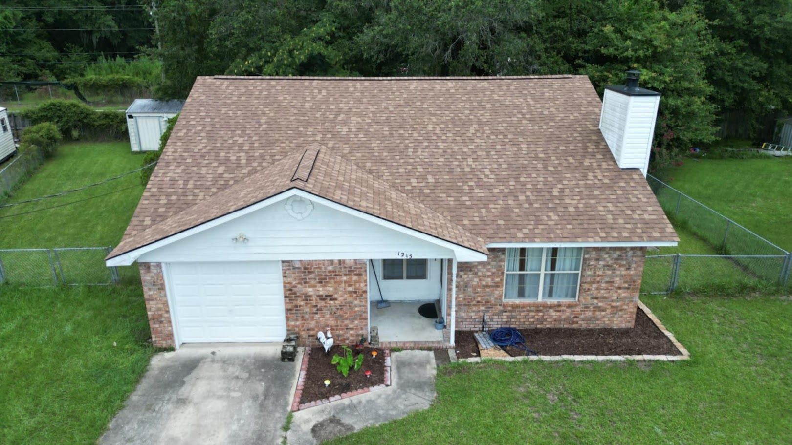 Brown brick house with a brown shingle roof, green lawn, white trim, and a chimney.
