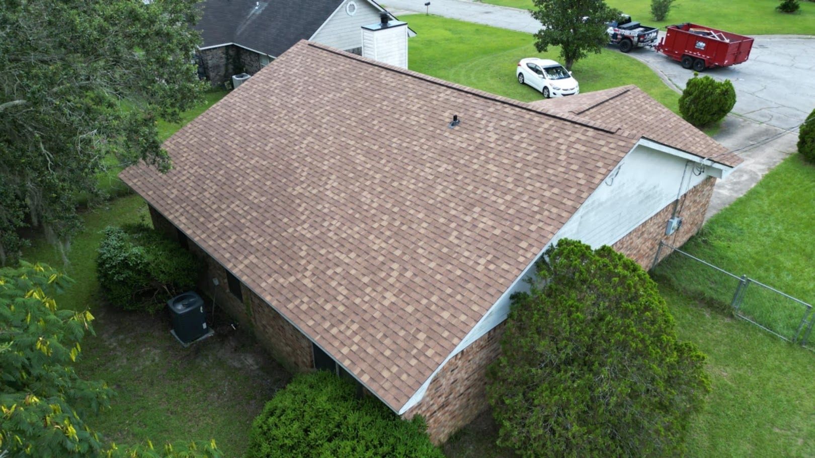 Aerial view of a brown-roofed brick house surrounded by green grass and trees.