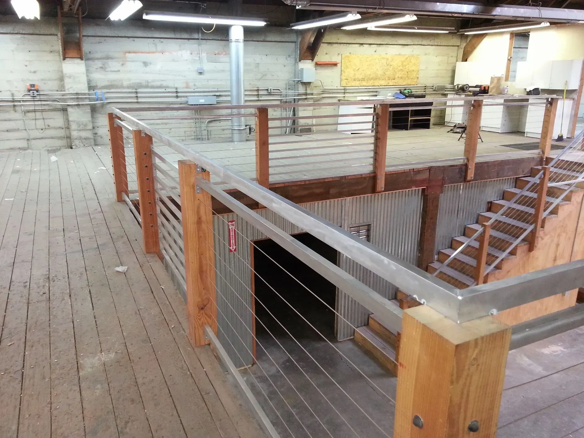 Interior view of a wooden second story with metal railings and stairs. Construction materials visible.