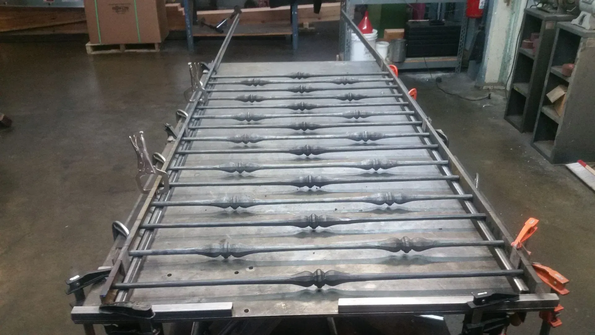 Metal railing frame clamped to a metal table in a workshop.