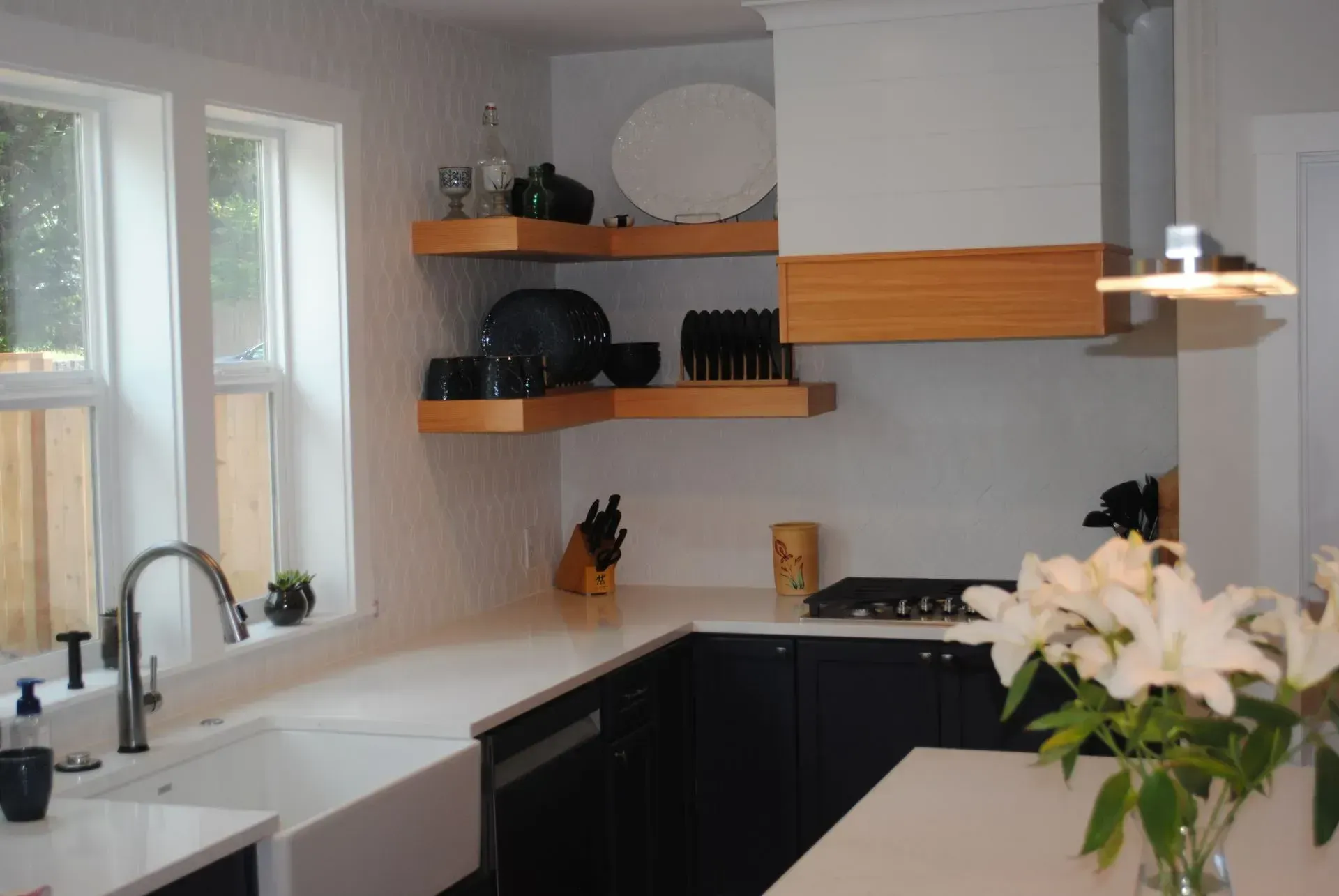 L-shaped kitchen with white countertops, dark blue cabinets, open shelving, and a white sink.