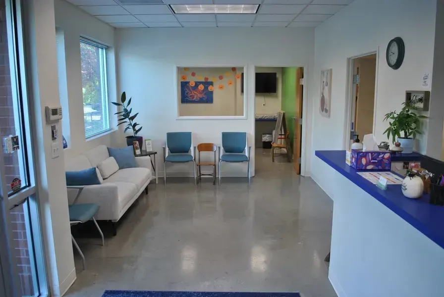 Waiting room with white sofa, blue chairs, reception desk, and doorway.