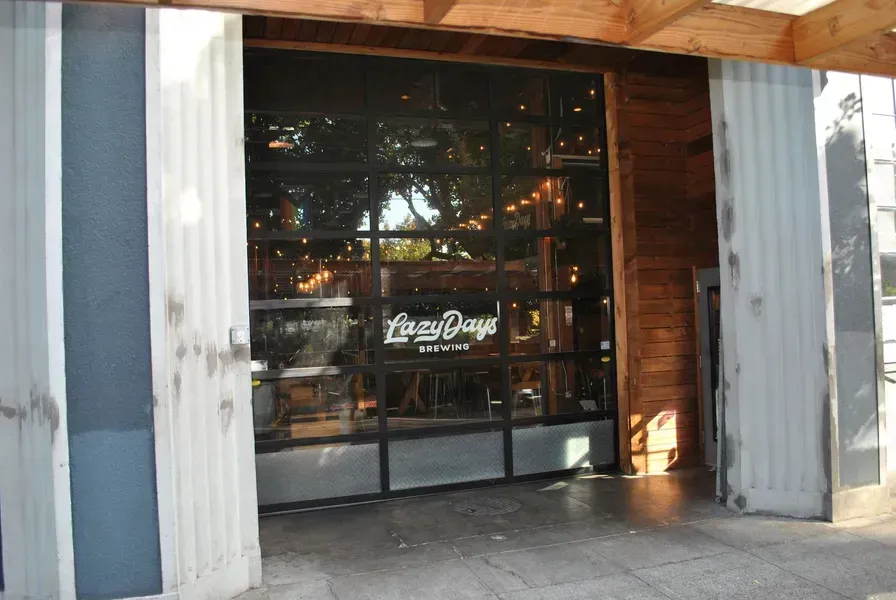 Open storefront with glass doors and warm lights inside, framed by wood and metal panels