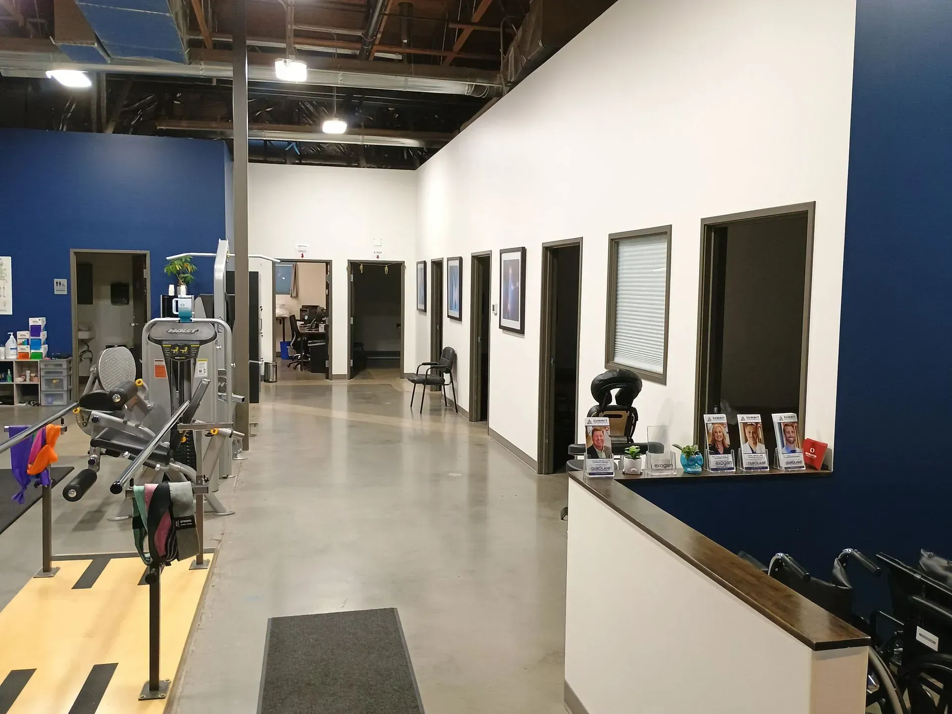 Interior view of a physical therapy clinic with equipment and a row of treatment rooms.