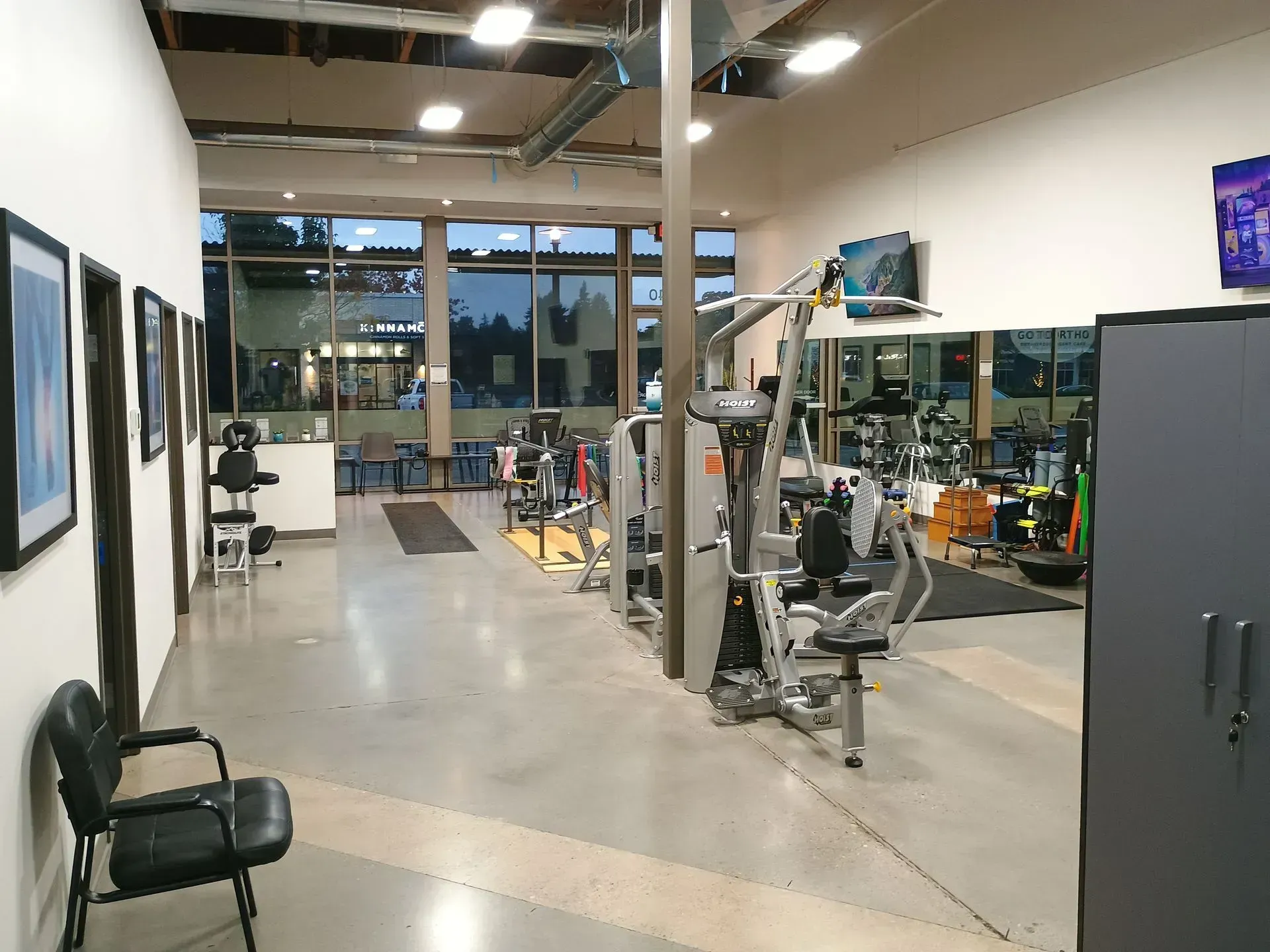 Gym interior with exercise equipment, including weight machines. A black chair sits in the foreground.