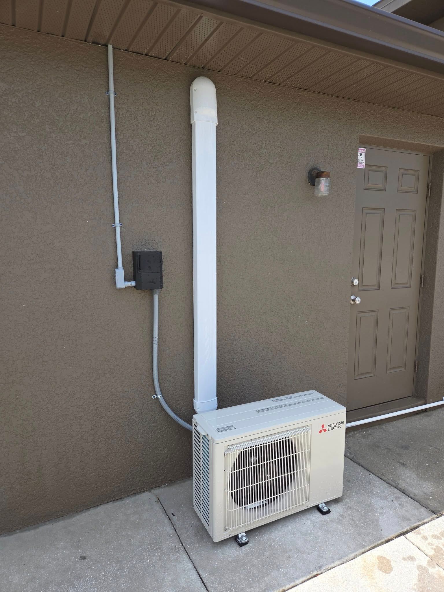 A white air conditioner is sitting on the side of a building next to a door.