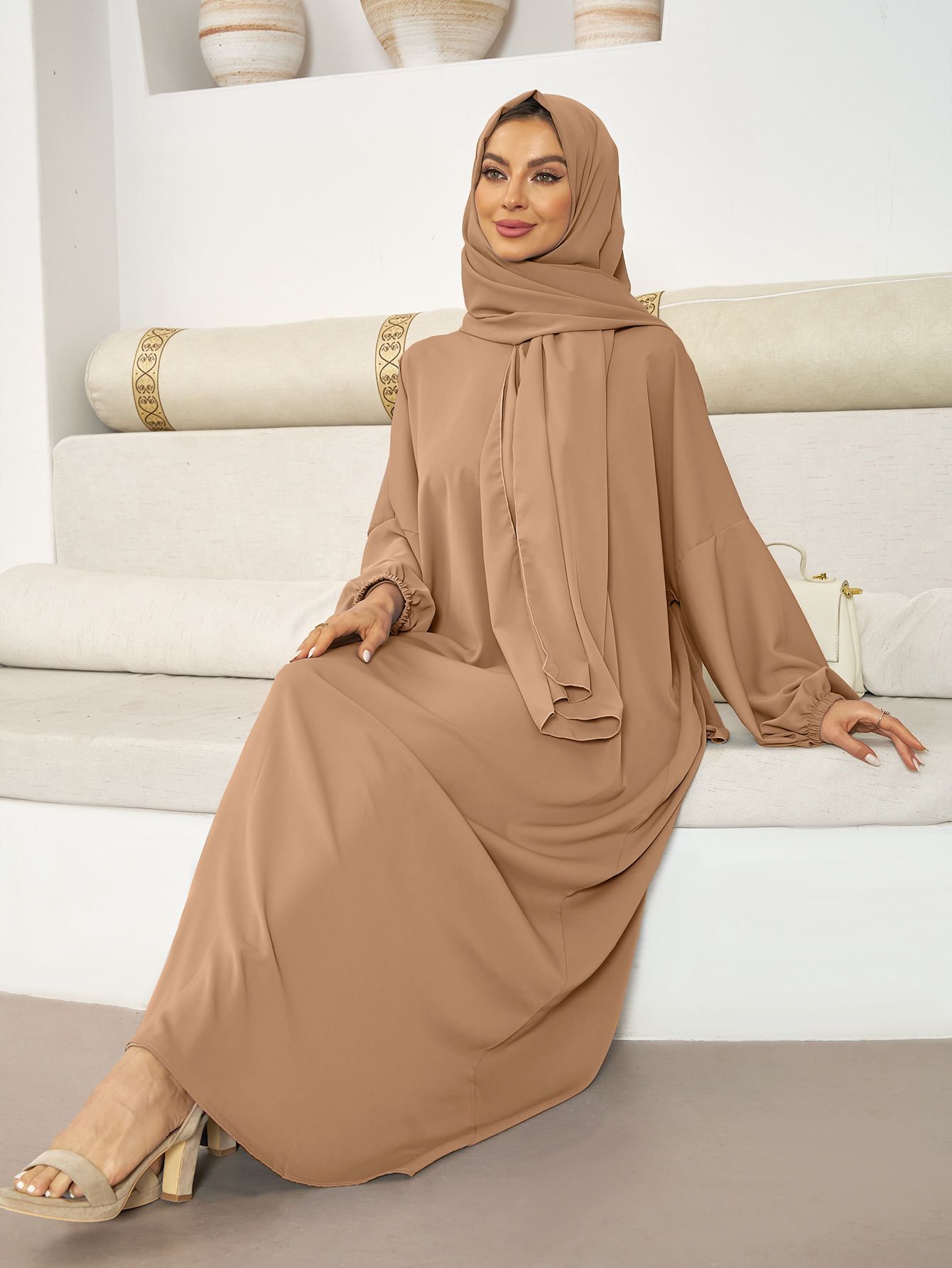 A woman in a blue dress and hijab is sitting on a couch.