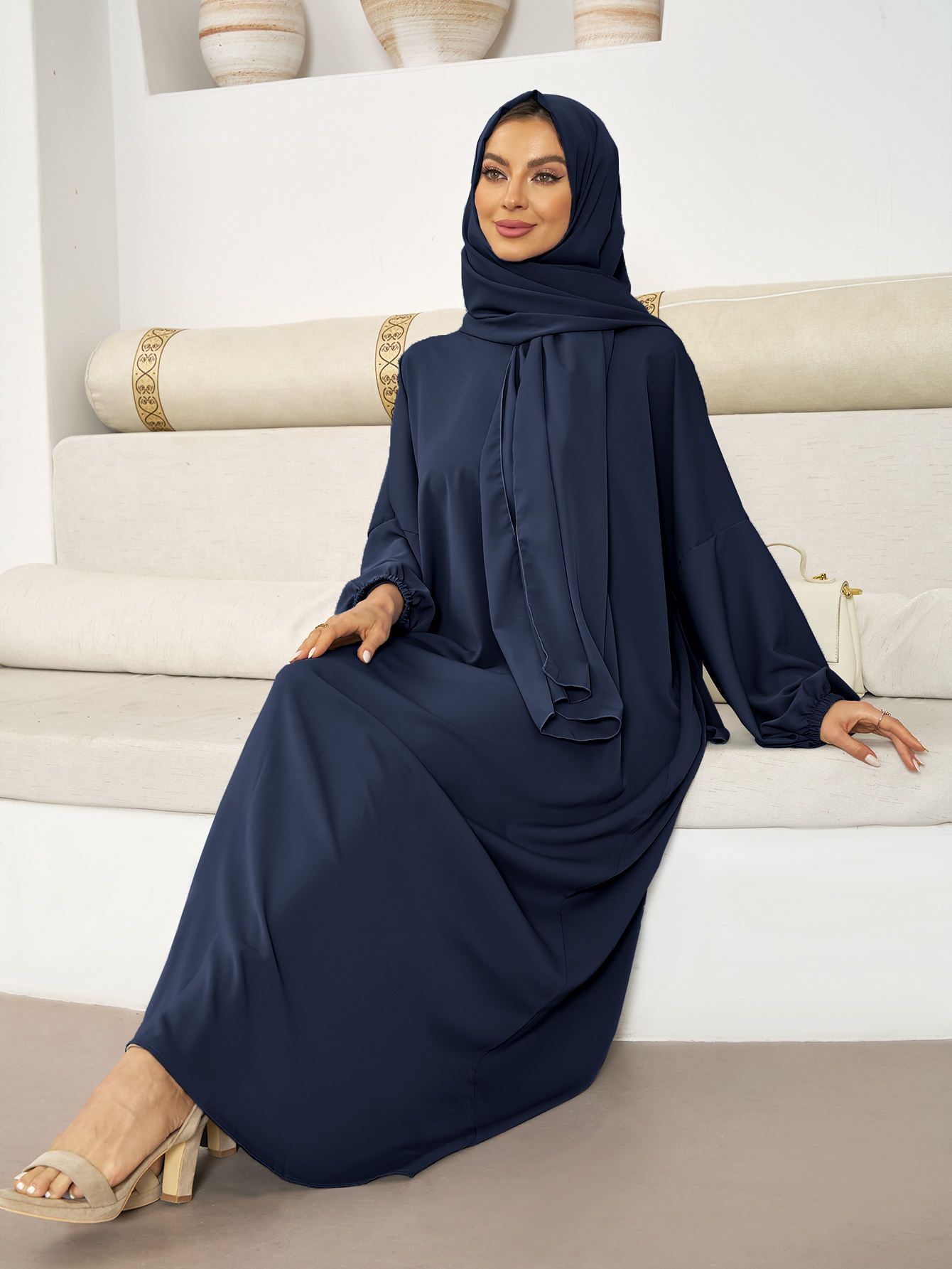 A woman in a blue dress and hijab is sitting on a couch.
