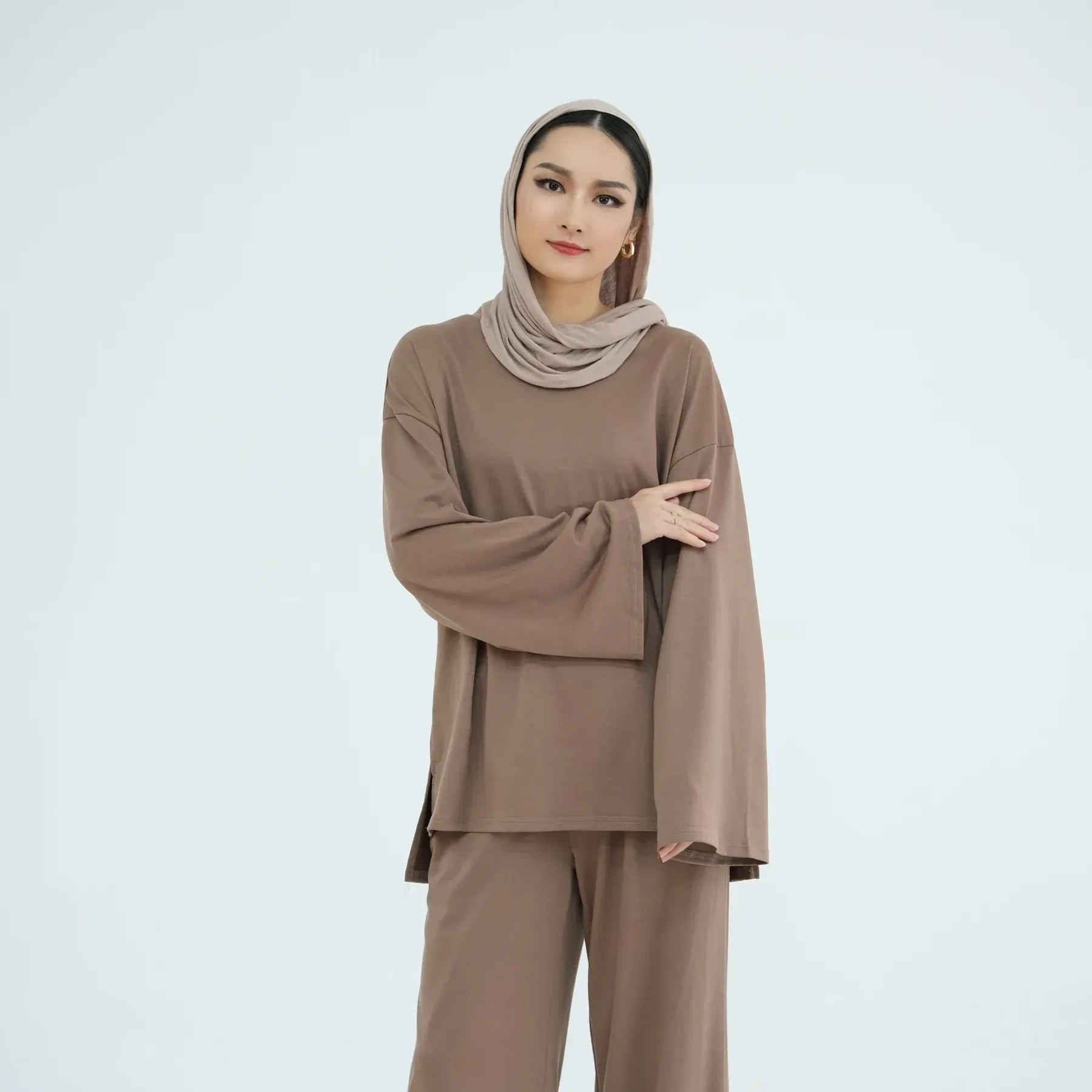 A woman wearing a hijab and a green shirt is standing on a white background.