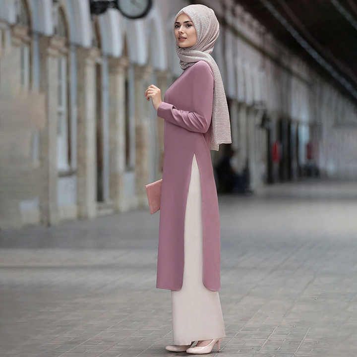 A woman wearing a hijab and a pink dress is standing on a sidewalk.