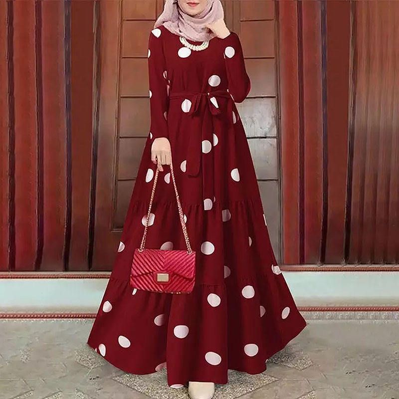 A woman is wearing a maroon dress with white polka dots and holding a red purse.
