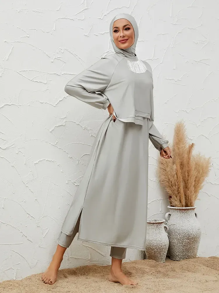 A woman wearing a hijab and a long dress is standing next to a vase.