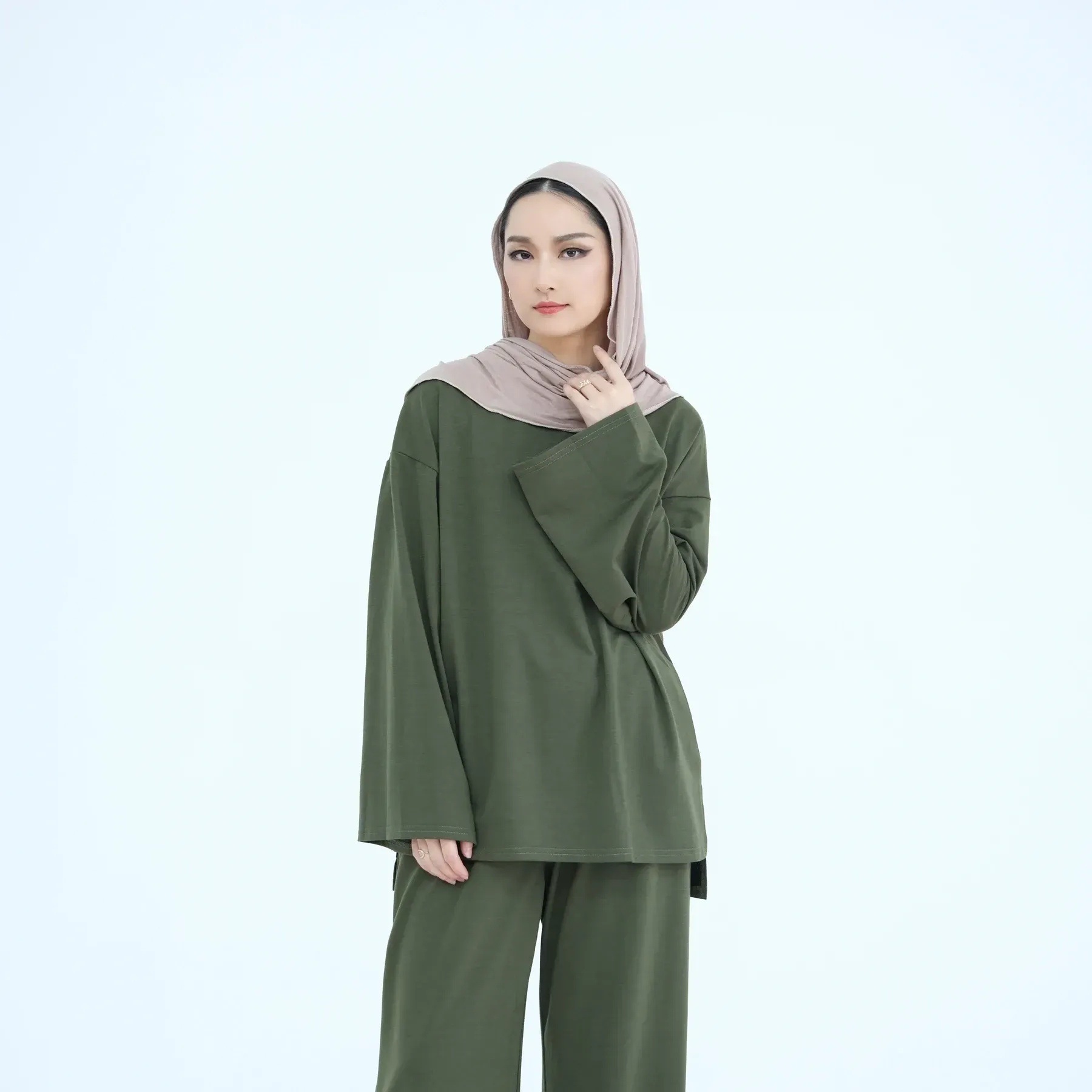 A woman wearing a hijab and a green shirt is standing on a white background.