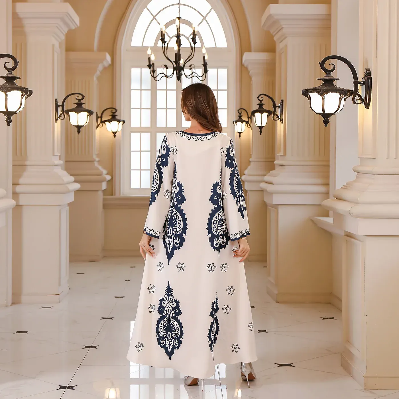 A woman in a long white and blue dress is standing in a hallway.