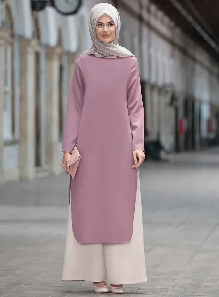 A woman wearing a hijab and a pink dress is standing on a sidewalk.