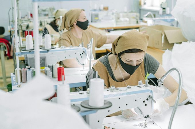 A woman wearing a mask is using a sewing machine in a factory.