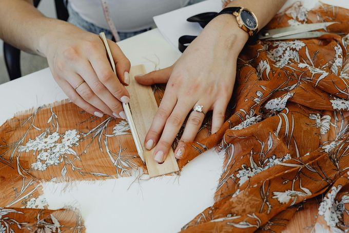 A woman is measuring a piece of fabric with a ruler and scissors.