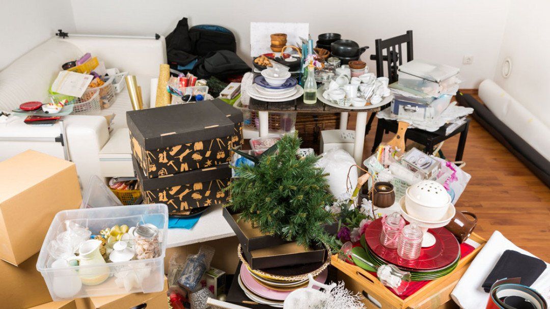 A messy living room with a lot of boxes and plates on the floor.