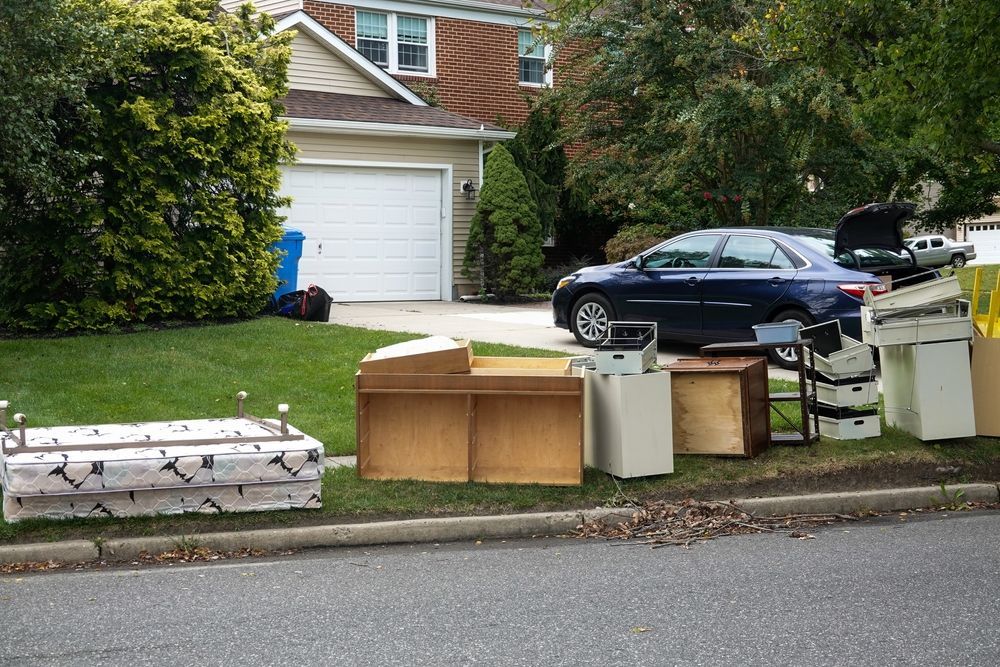 A car is parked in front of a house with a bunch of junk on the side of the road