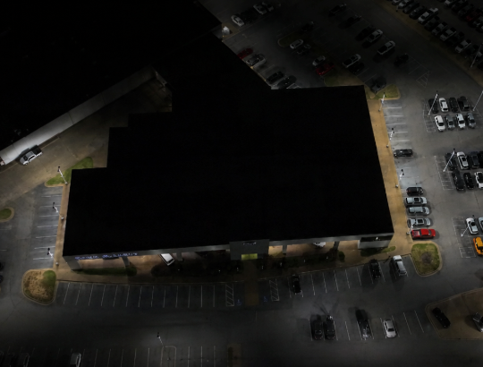 Aerial view of a dark building at night, surrounded by parked cars and lit parking lots.