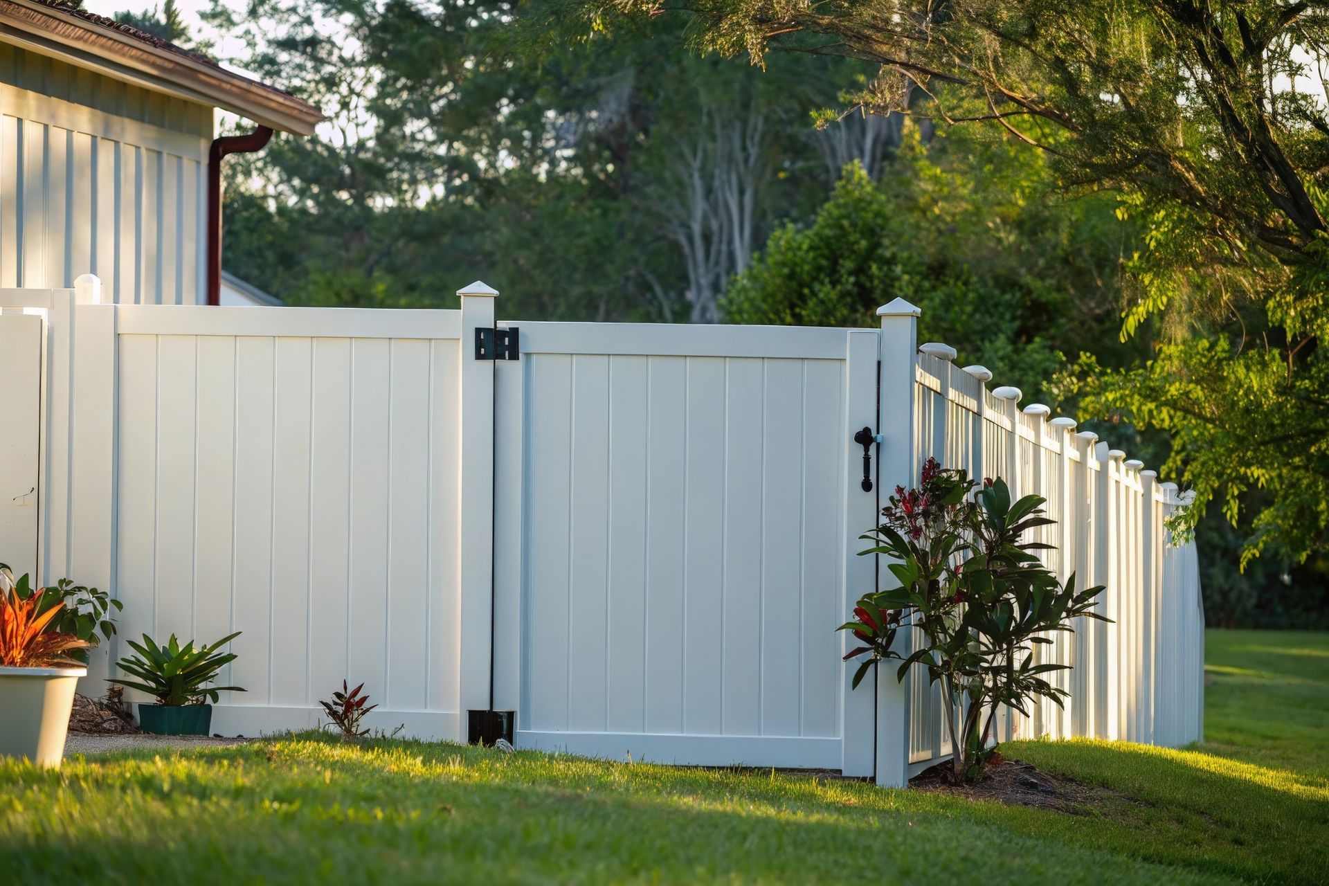 White vinyl privacy fence with a gate and plants along a landscaped yard.