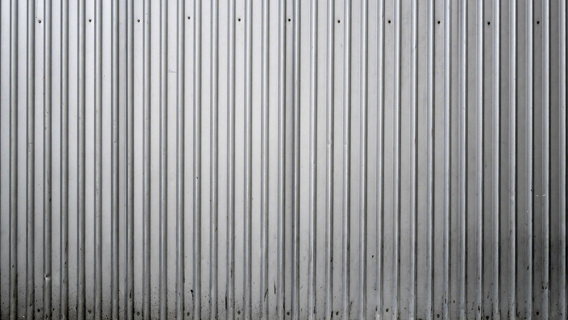 Close-up of a corrugated metal wall with vertical ridges and a weathered base.