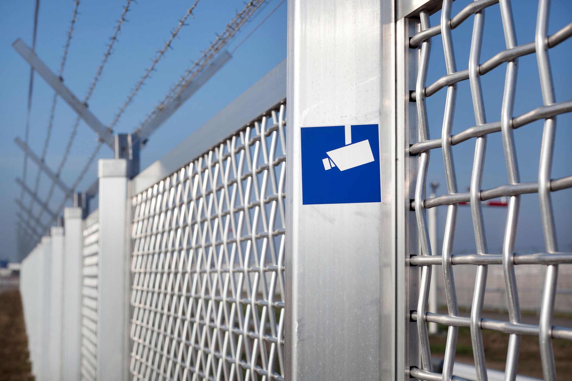 A security camera sign on a metal fence with barbed wire.