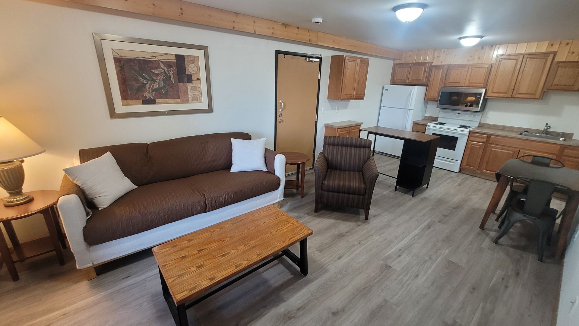 Living area with kitchen, couch, armchair, table, and wooden cabinets.