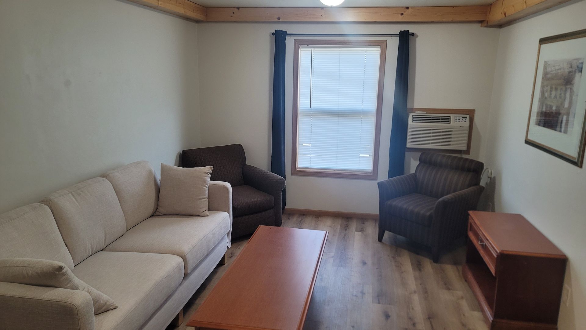 Living room with beige couch, two armchairs, a coffee table, and a window with curtains.