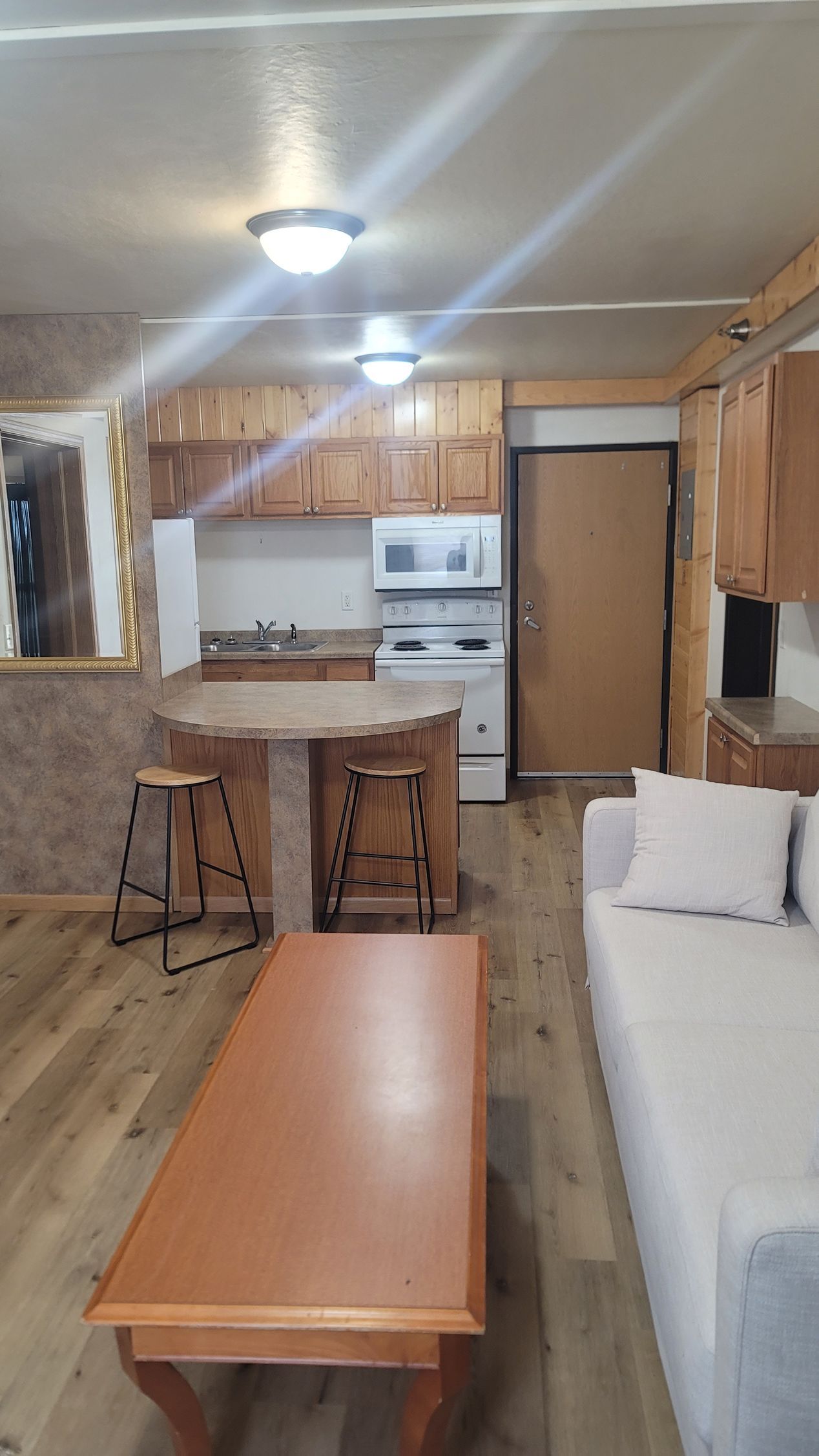Small kitchen and living area, with light wood cabinets, an island, and a beige sofa.