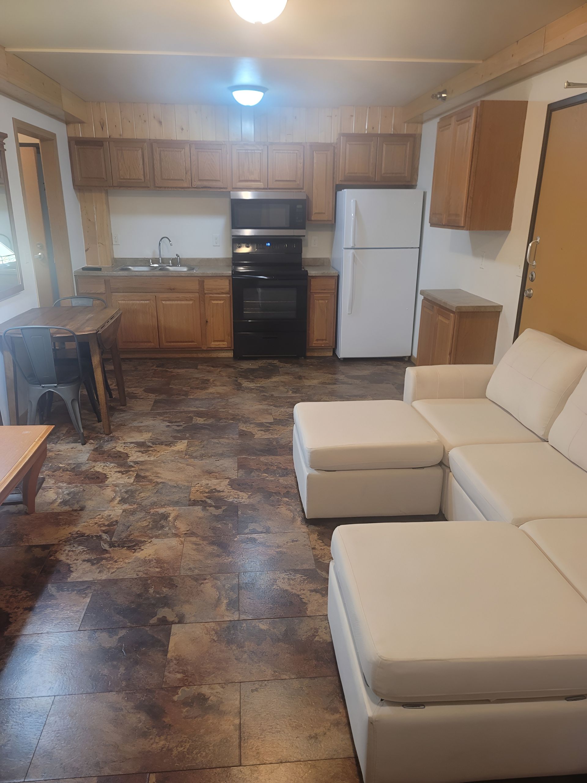 Bedroom with a bed, shelf unit, and window. Pale walls, wood trim, and a small painting are visible.