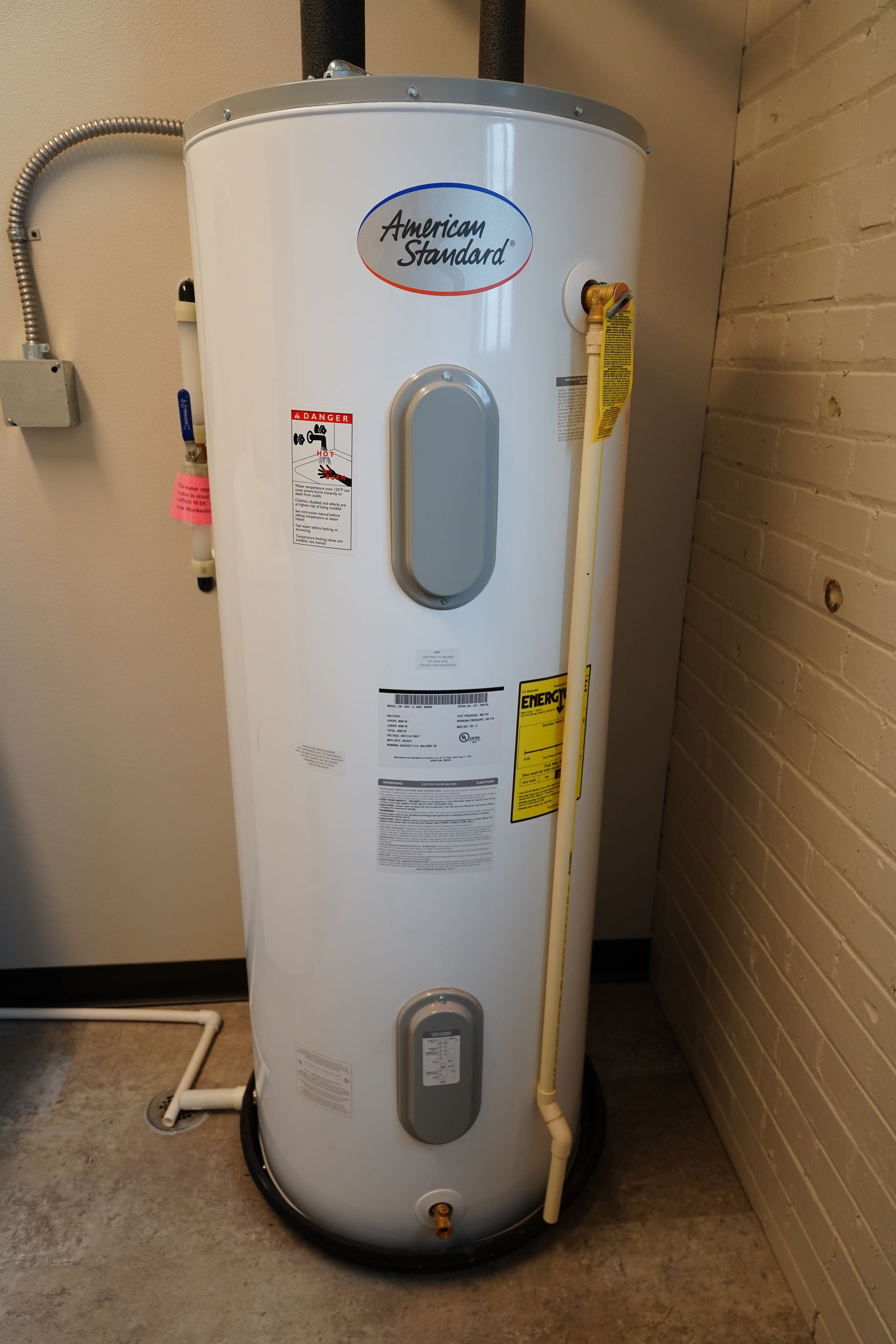 White American Standard water heater in a concrete-walled room.