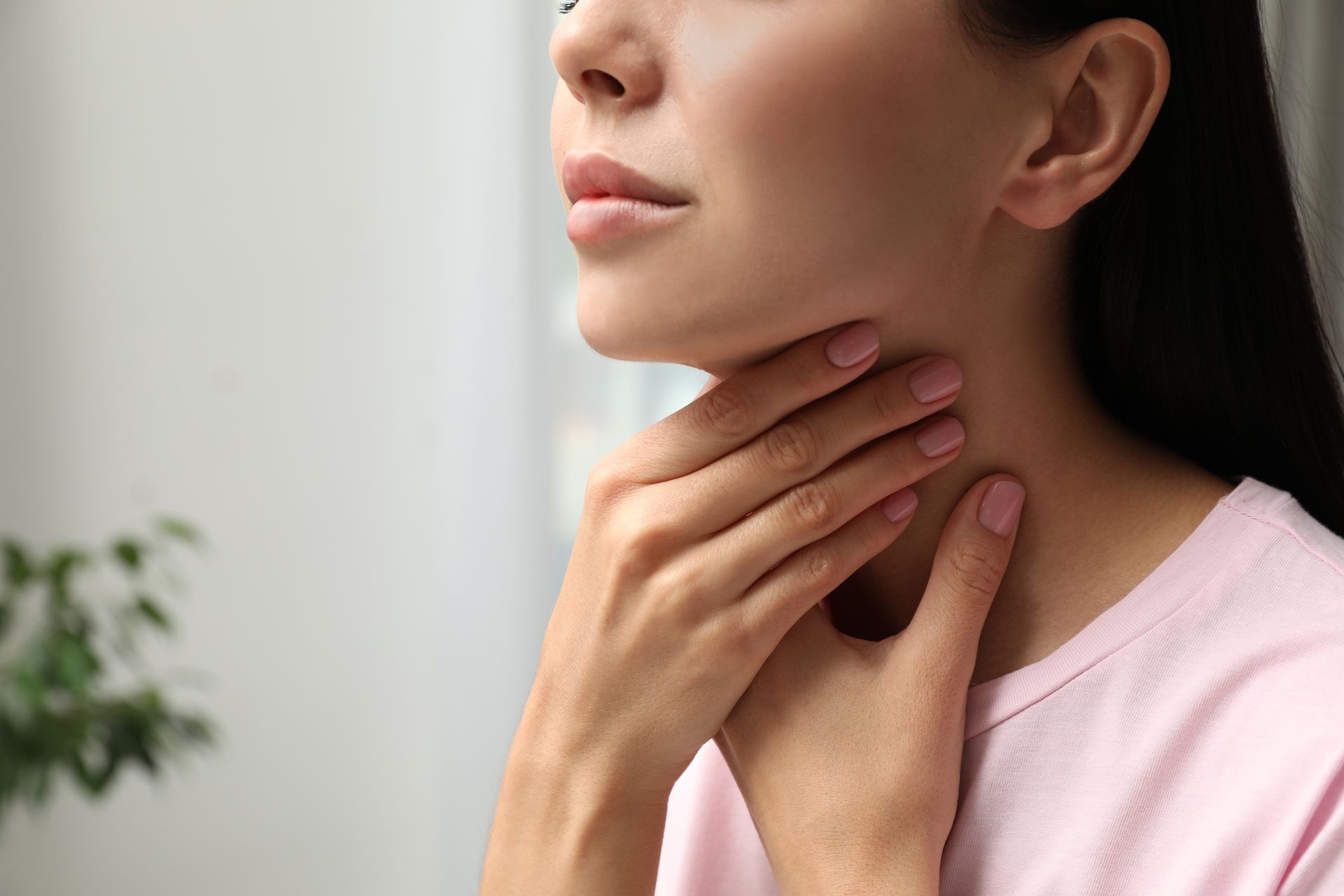 A woman is holding her neck with her hands because she has a sore throat.