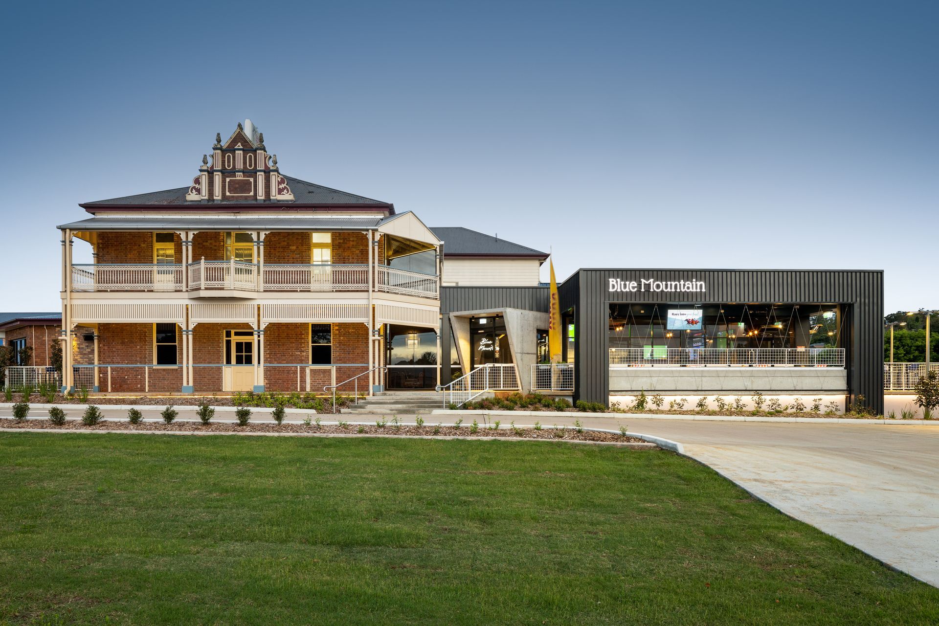 Two-story brick building with veranda next to modern structure; grassy lawn in front;