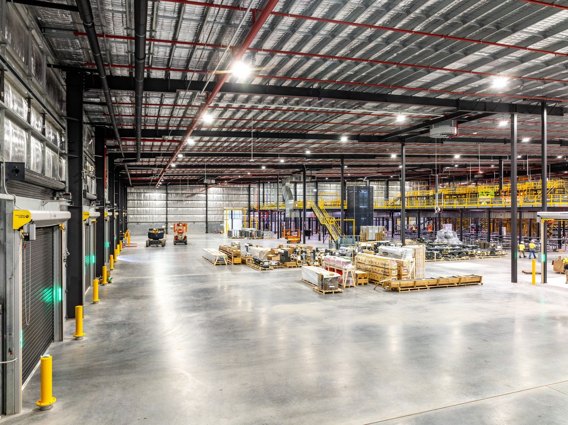 Warehouse interior with machinery, goods, and a high ceiling with overhead lighting.
