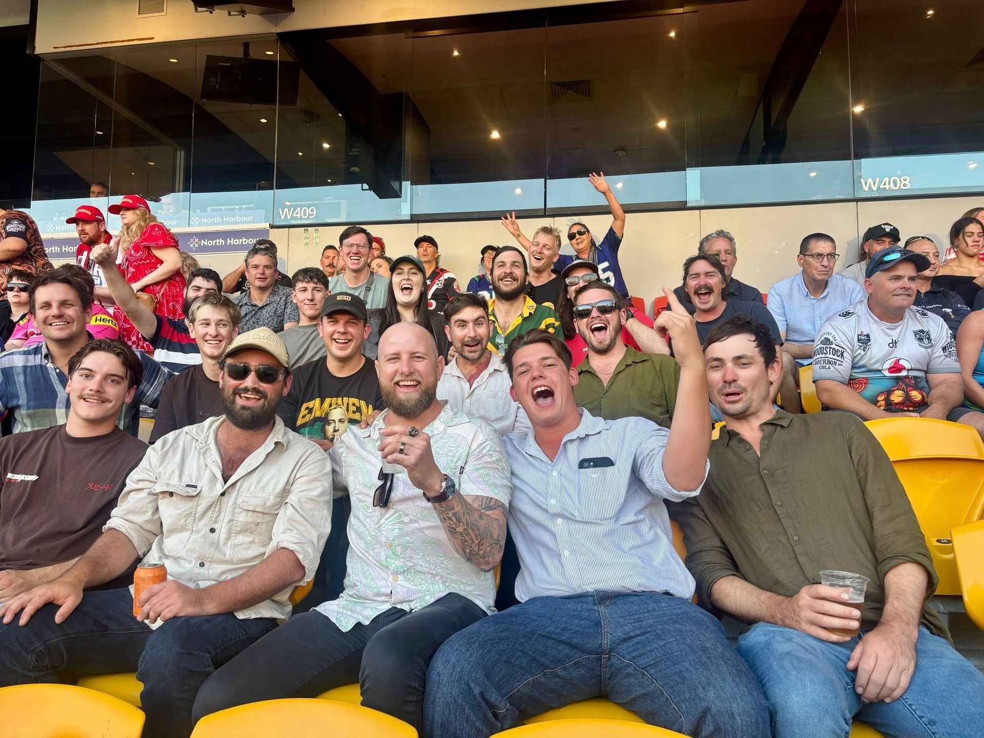 Group of excited fans cheering in a stadium, some with arms raised and open mouths.