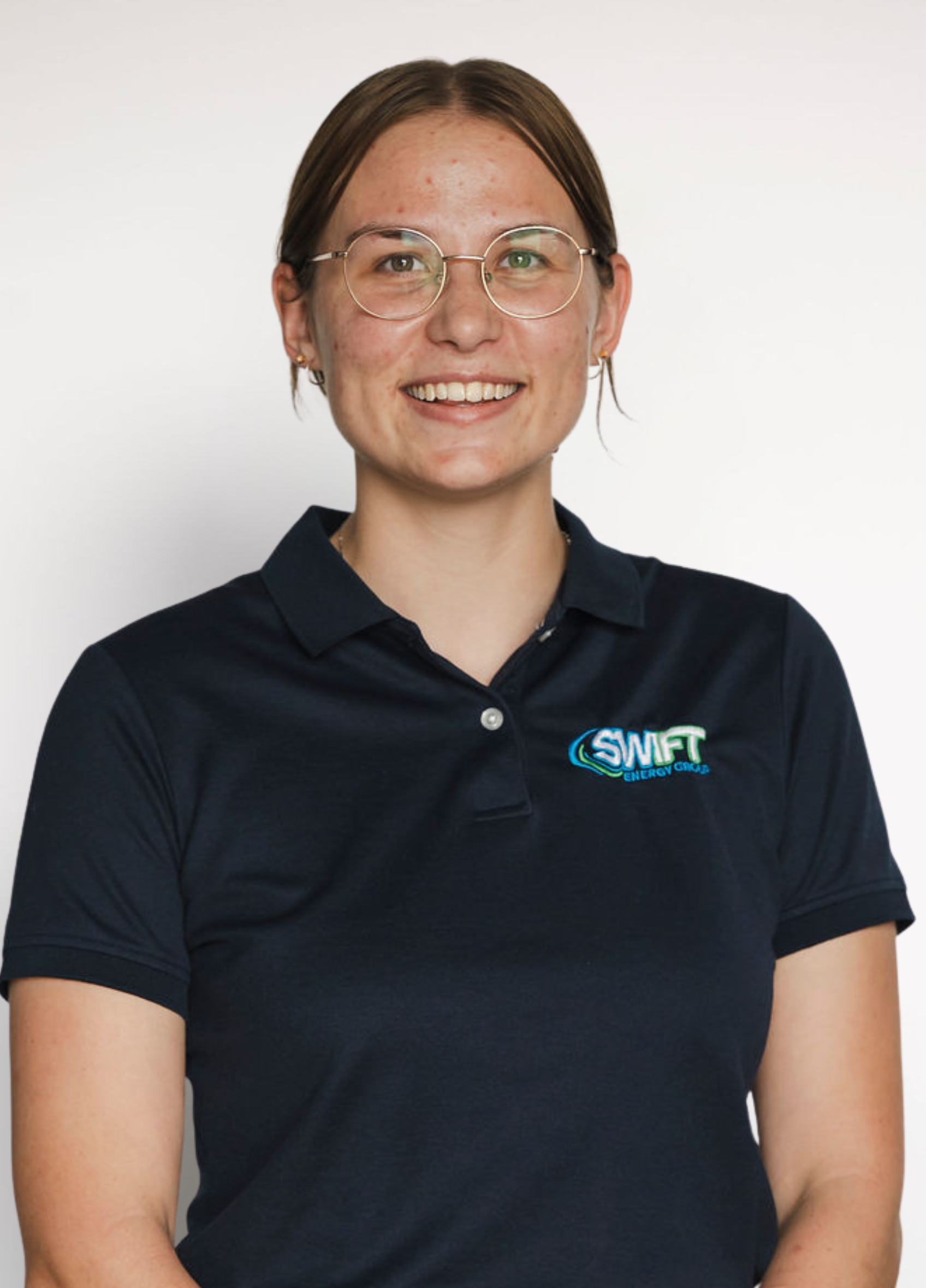 Woman with glasses and arms crossed, wearing a blue shirt with a logo, smiling, white background.
