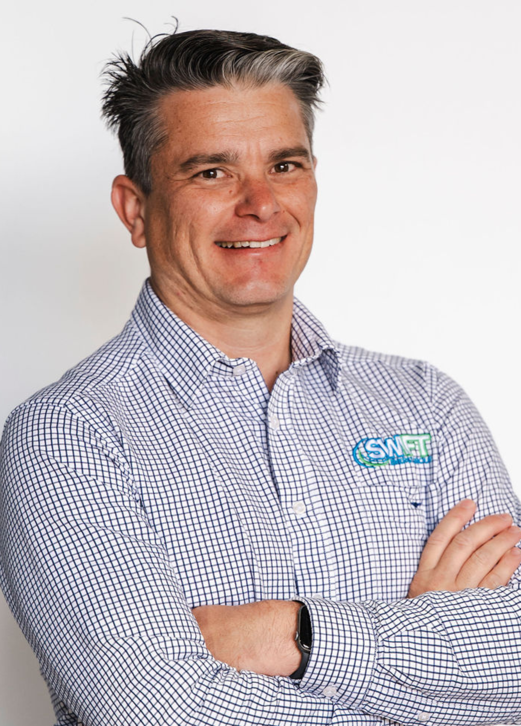Man with gray hair, wearing a patterned button-down shirt, arms crossed, smiling.