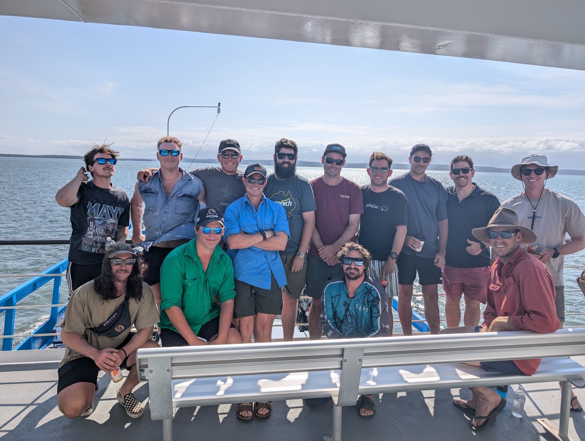 Group of people on a boat posing for a photo, with blue water and sky in the background.