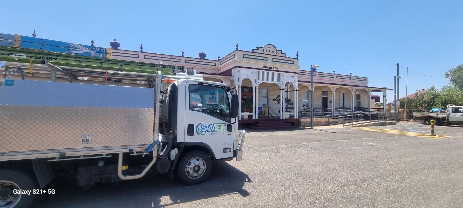 Truck parked in front of an old white building with a porch.