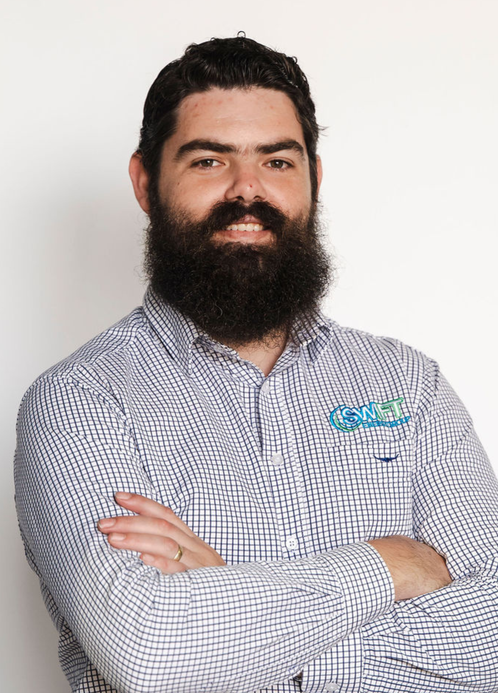 Man with a full beard and arms crossed, wearing a blue patterned shirt, smiles.