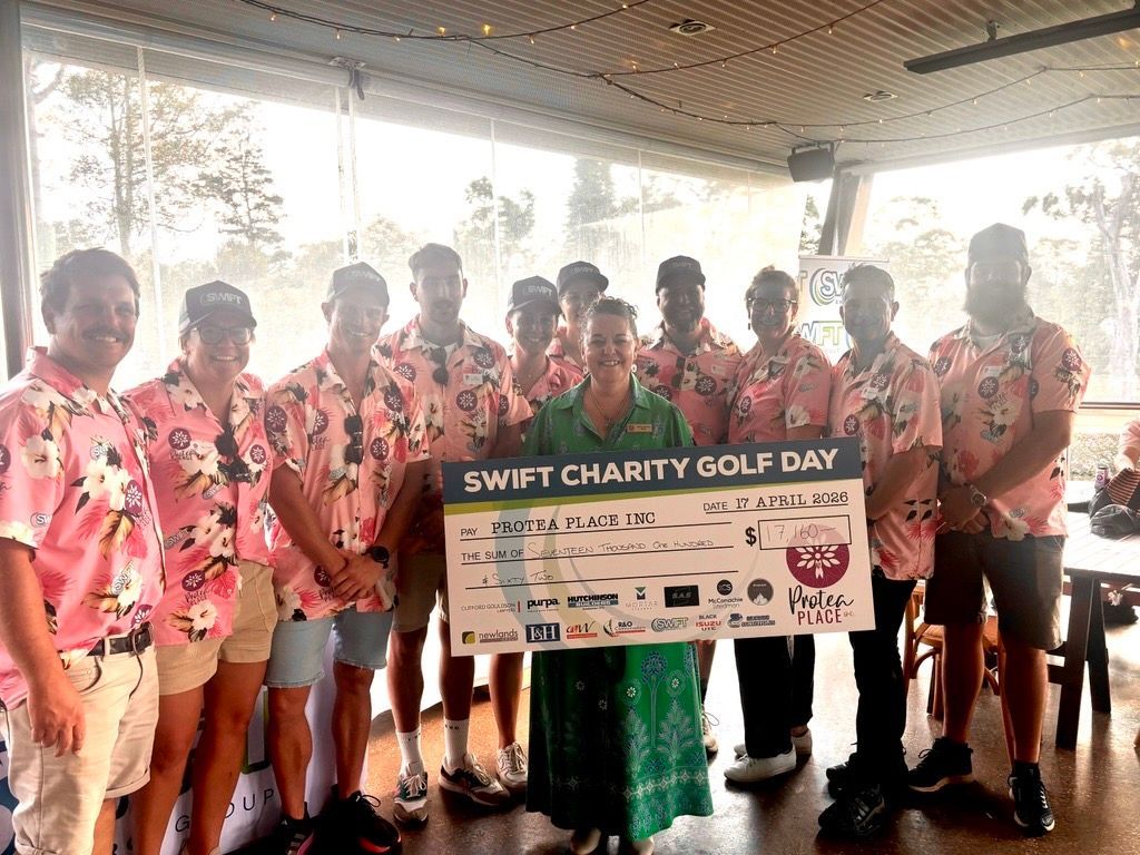 Group holding a “Swift Charity Golf Day” banner in a covered outdoor venue.