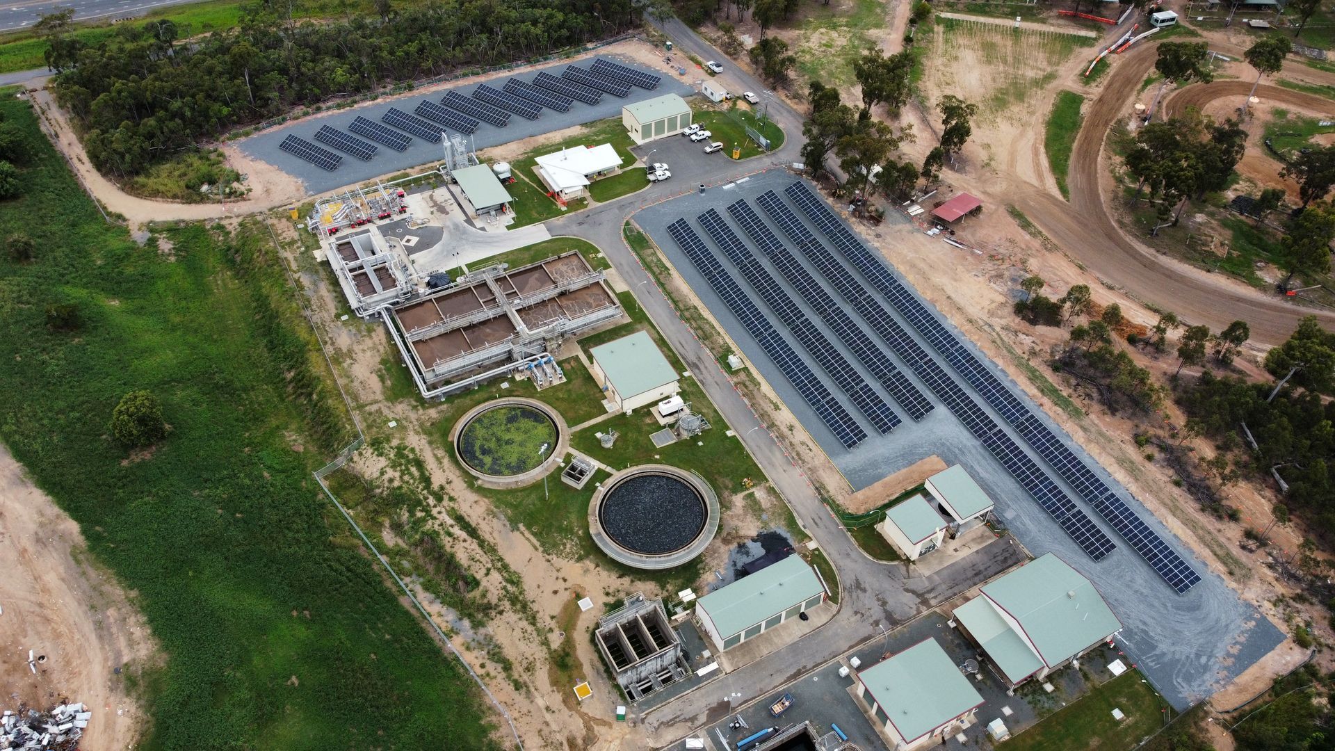 Aerial view of a wastewater treatment plant with solar panels and various processing structures.