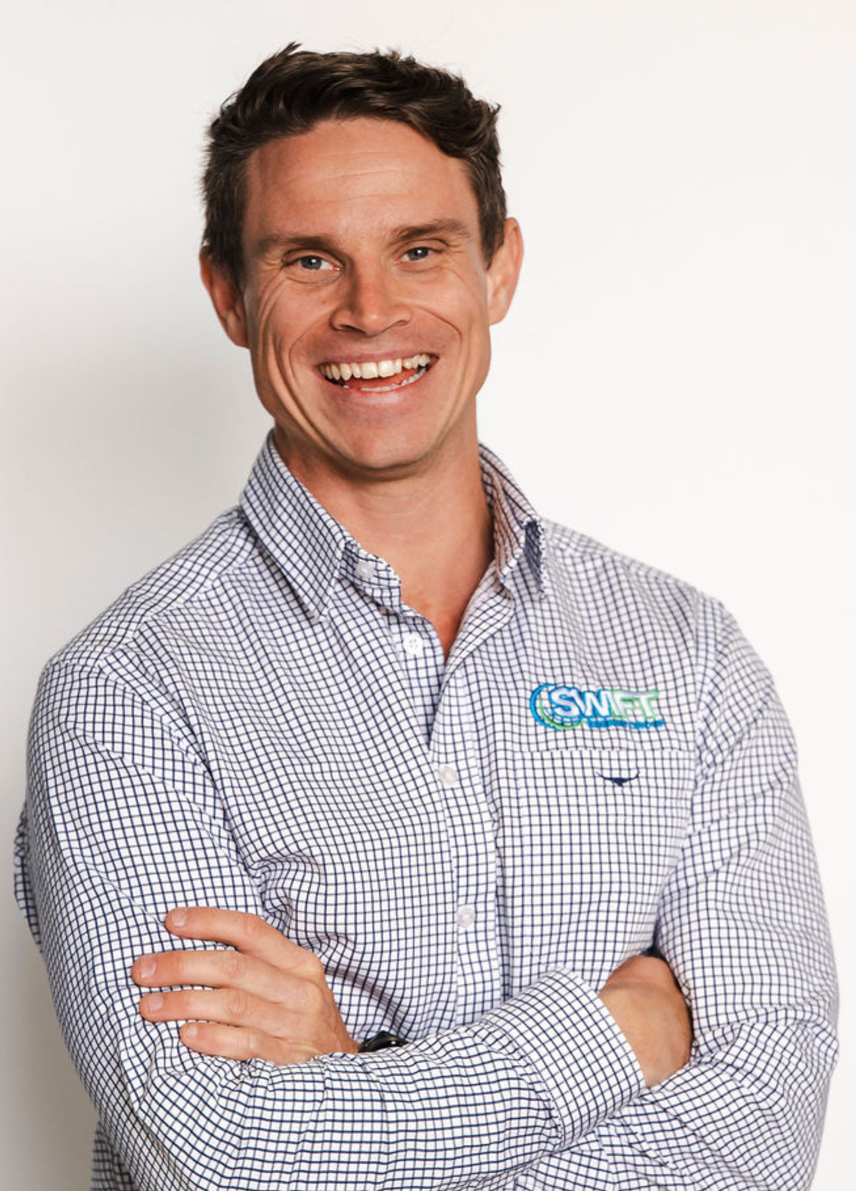 Man with crossed arms smiling in a blue and white checkered shirt.